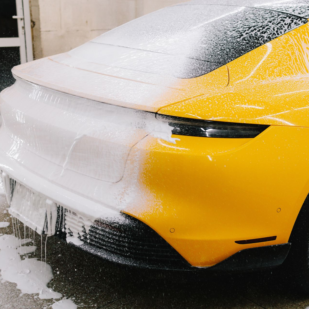 Yellow sports car being washed, covered in white foam.