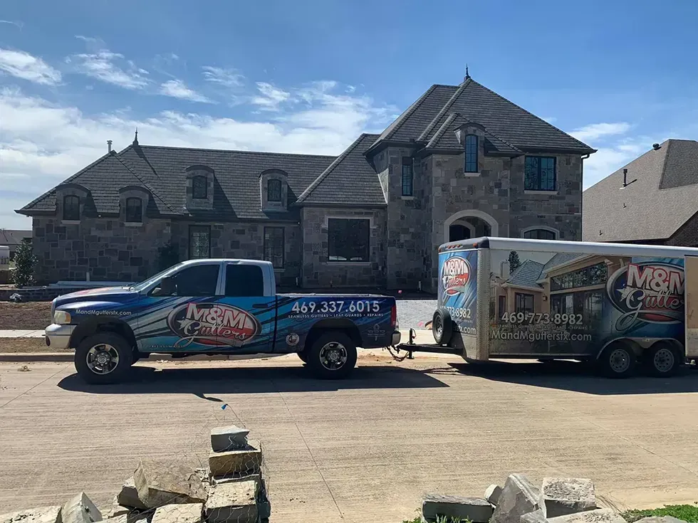 A truck and trailer are parked in front of a large house.