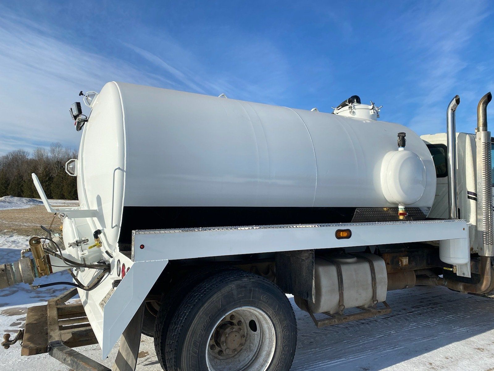 A white truck with a large tank on the back is parked in the snow.