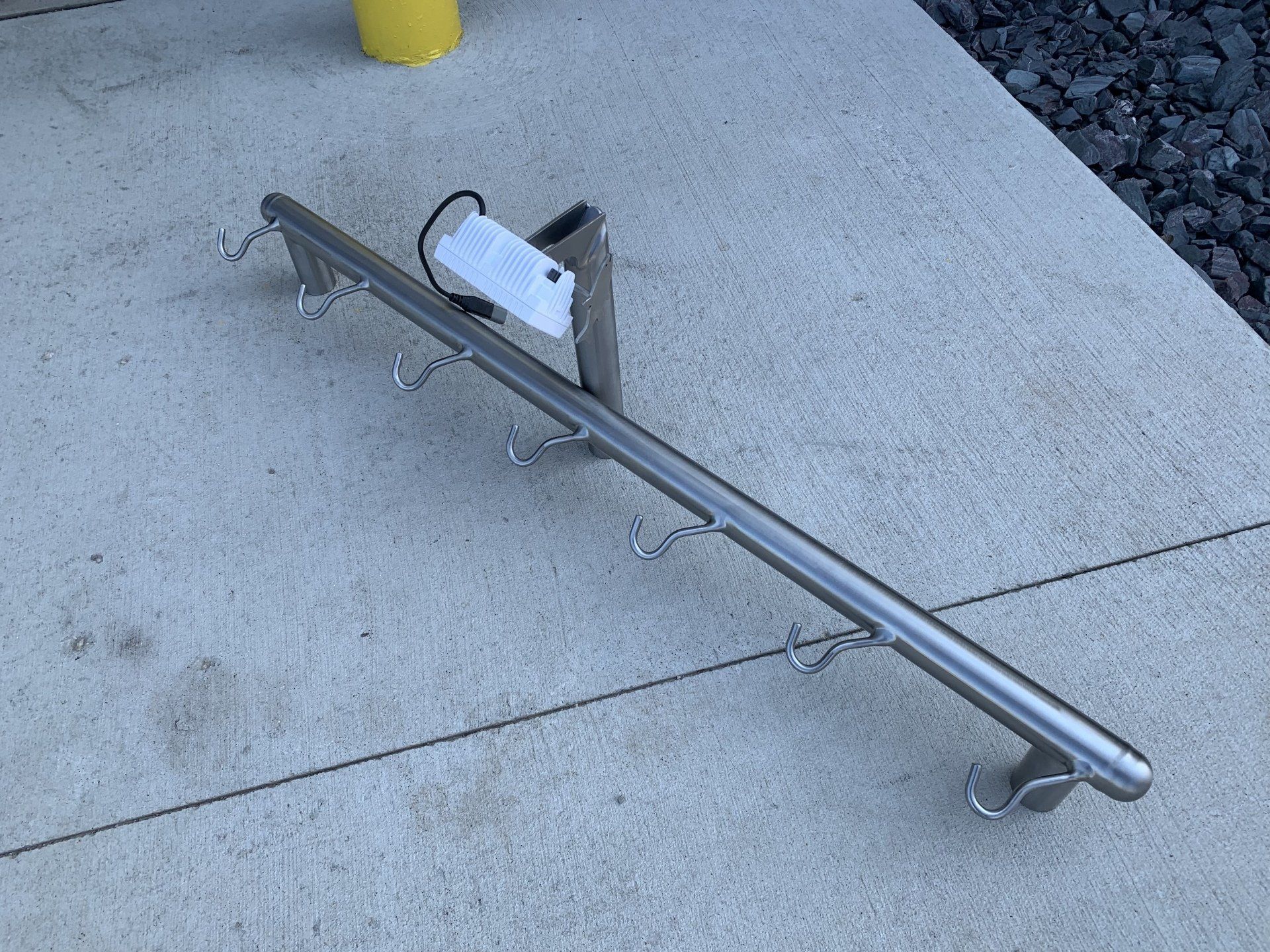 A stainless steel railing with hooks is sitting on a concrete surface.