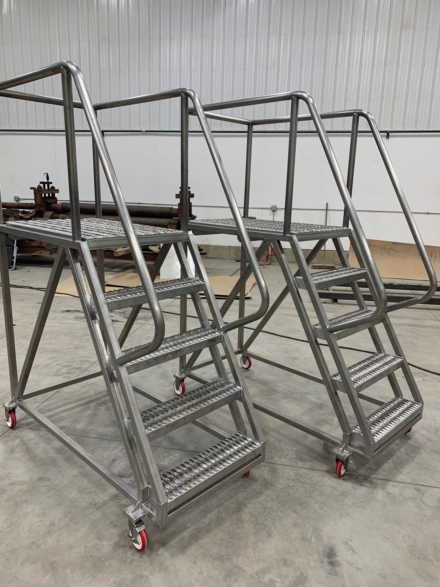 Two stainless steel stairs with wheels are sitting next to each other in a warehouse.