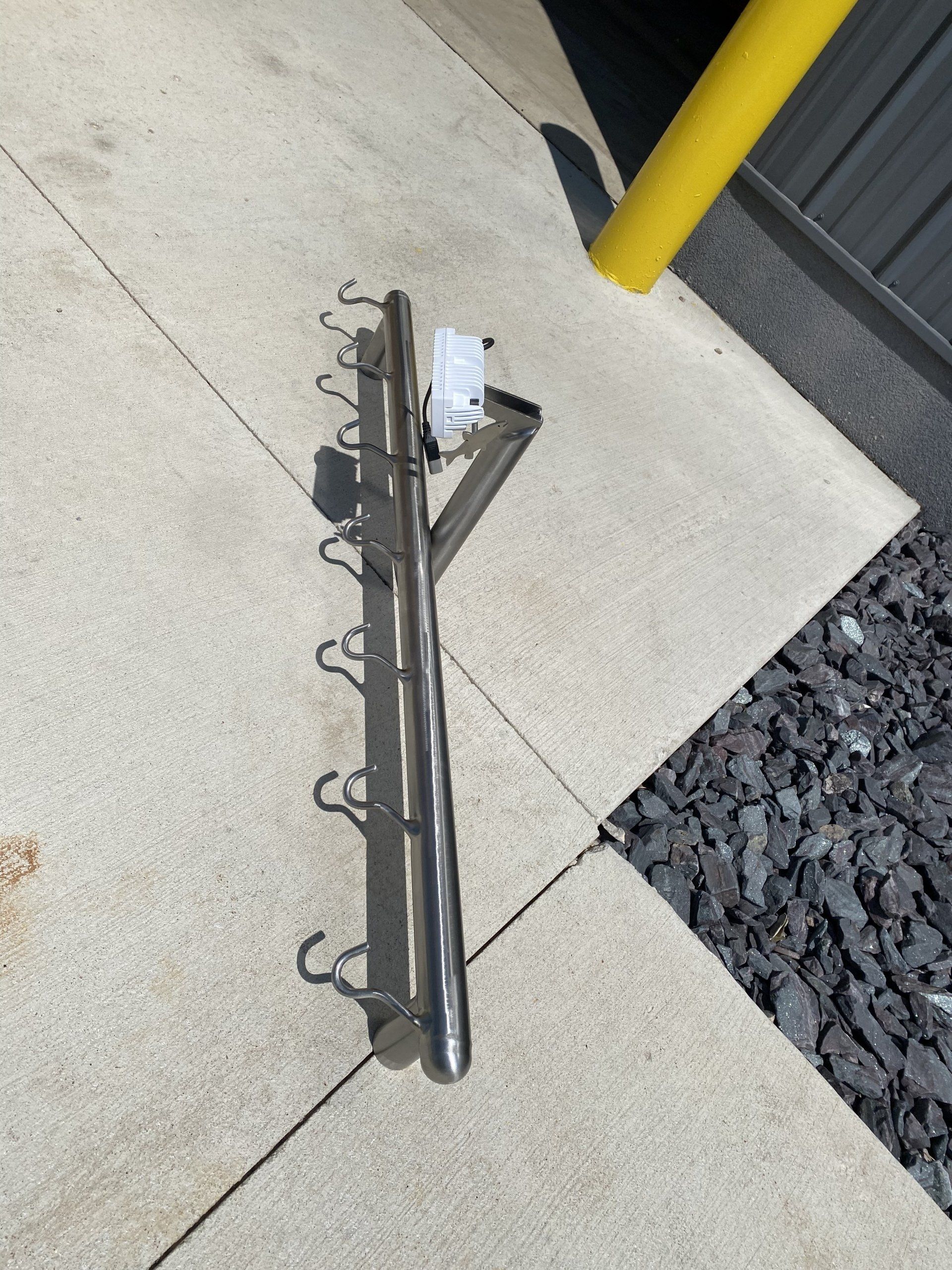A stainless steel hook on a sidewalk with a yellow pole in the background