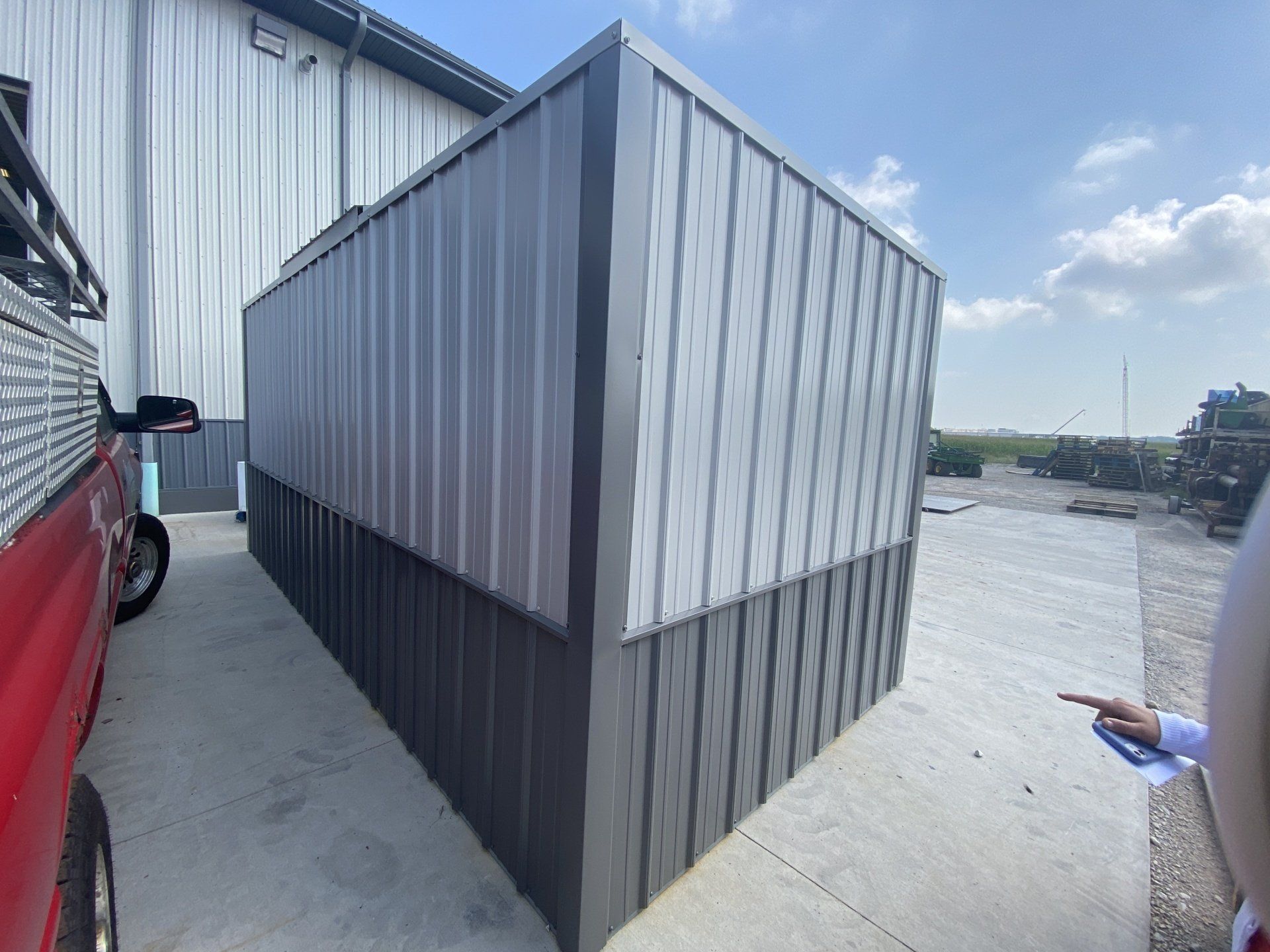 A red truck is parked in front of a large metal building.