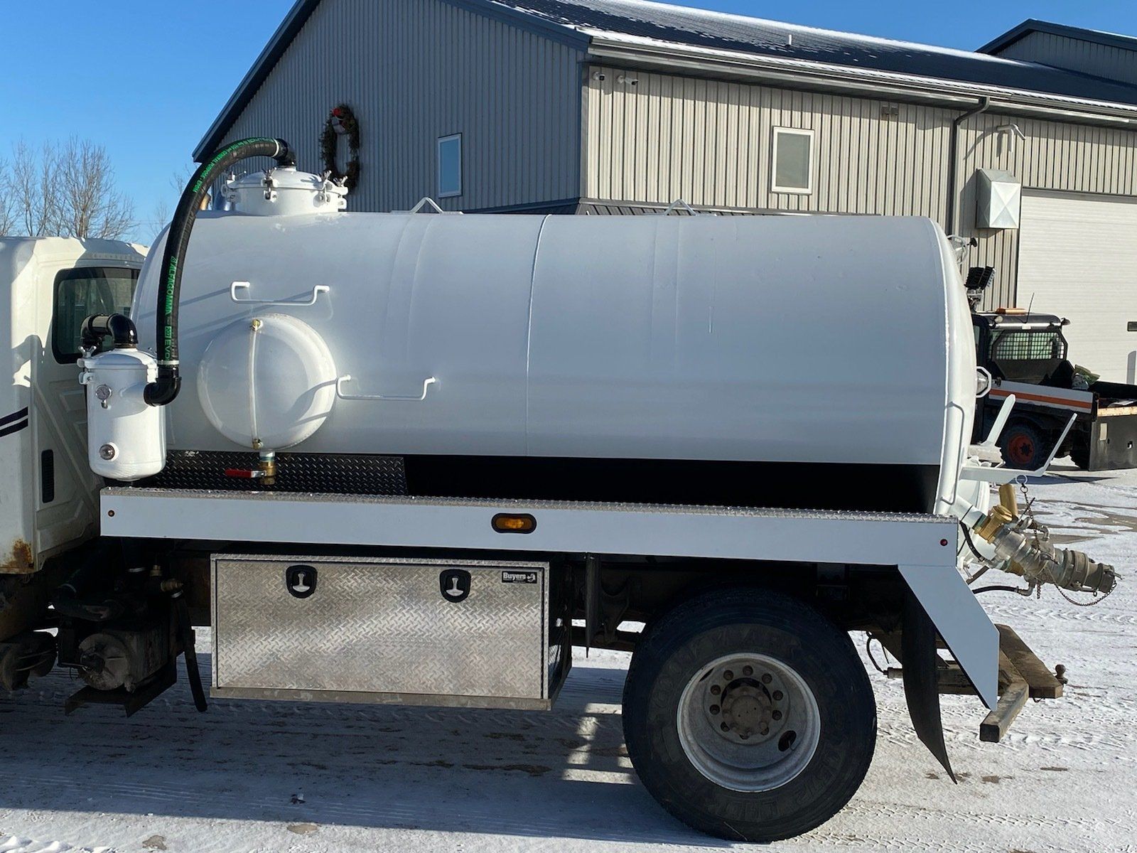 A white vacuum truck is parked in front of a building
