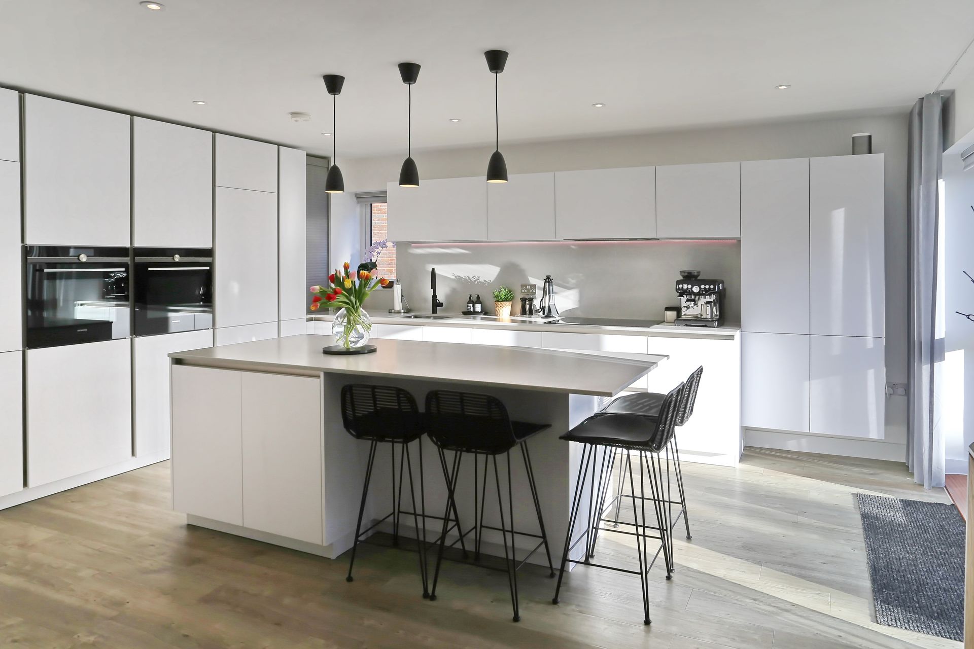 A modern, handleless kitchen with natural lighting, white cabinets and a large island .