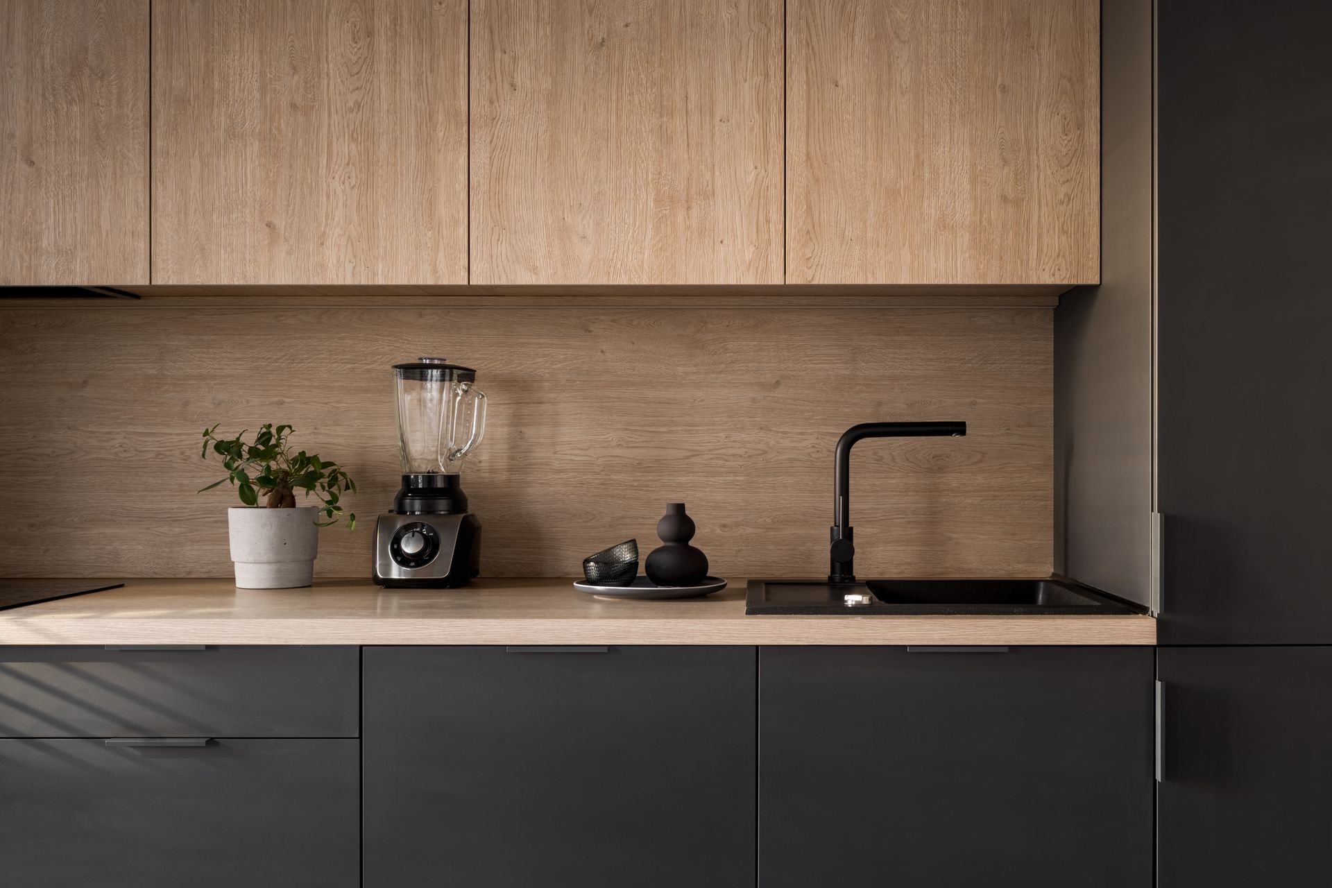 A black and wood kitchen with a black tap and small appliances on the counter