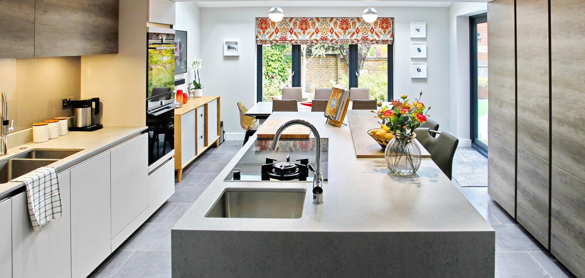 Modern kitchen with white countertops, island, and wood cabinets. Dining area with garden view.