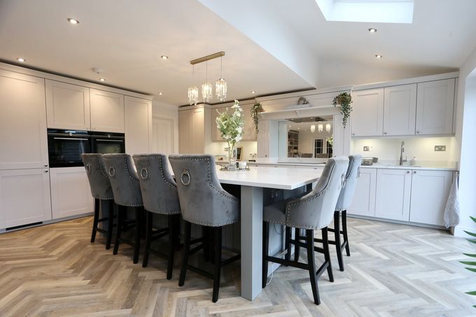 Modern white kitchen with large island, gray bar stools, herringbone floor, and recessed lighting.