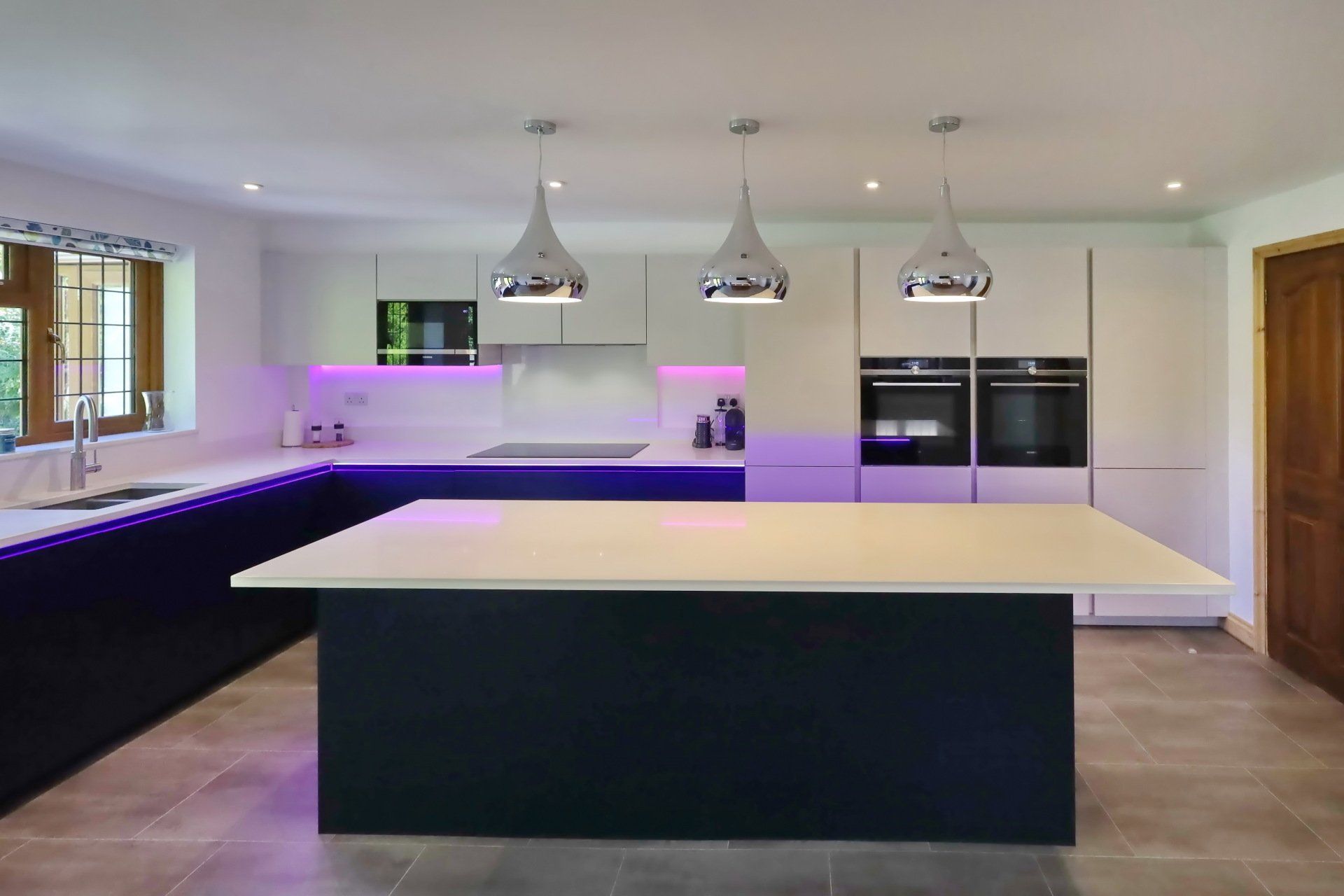 A modern kitchen with an island, blue units and a white marble worktop, designed by exact kitchens