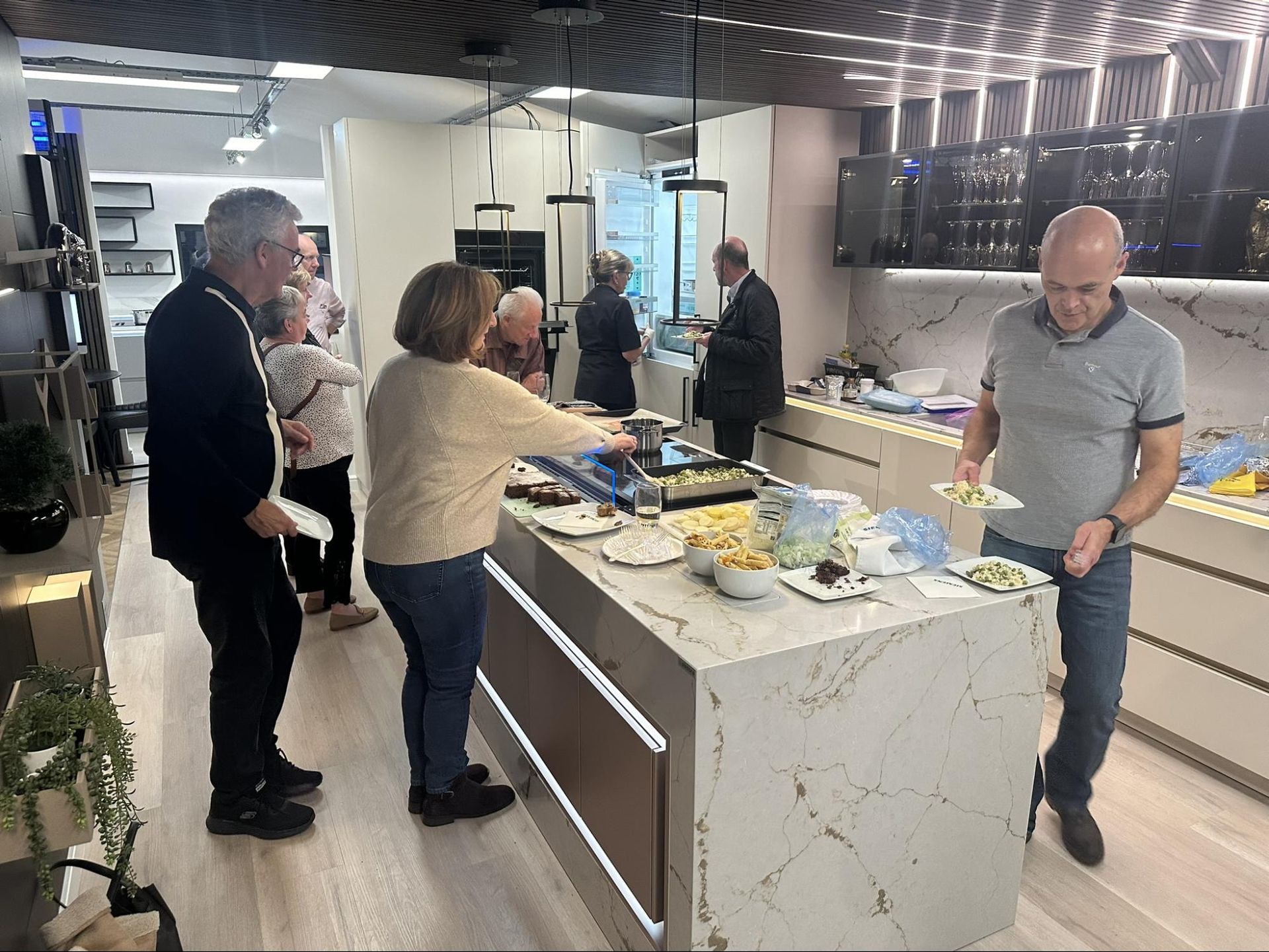 A group of people are standing around a kitchen island at exact Kitchens showroom in Barkham.