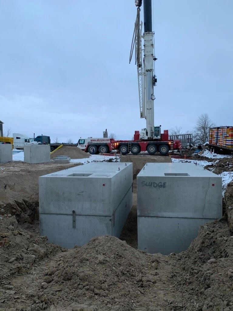 A large crane is lifting concrete blocks in a dirt field.