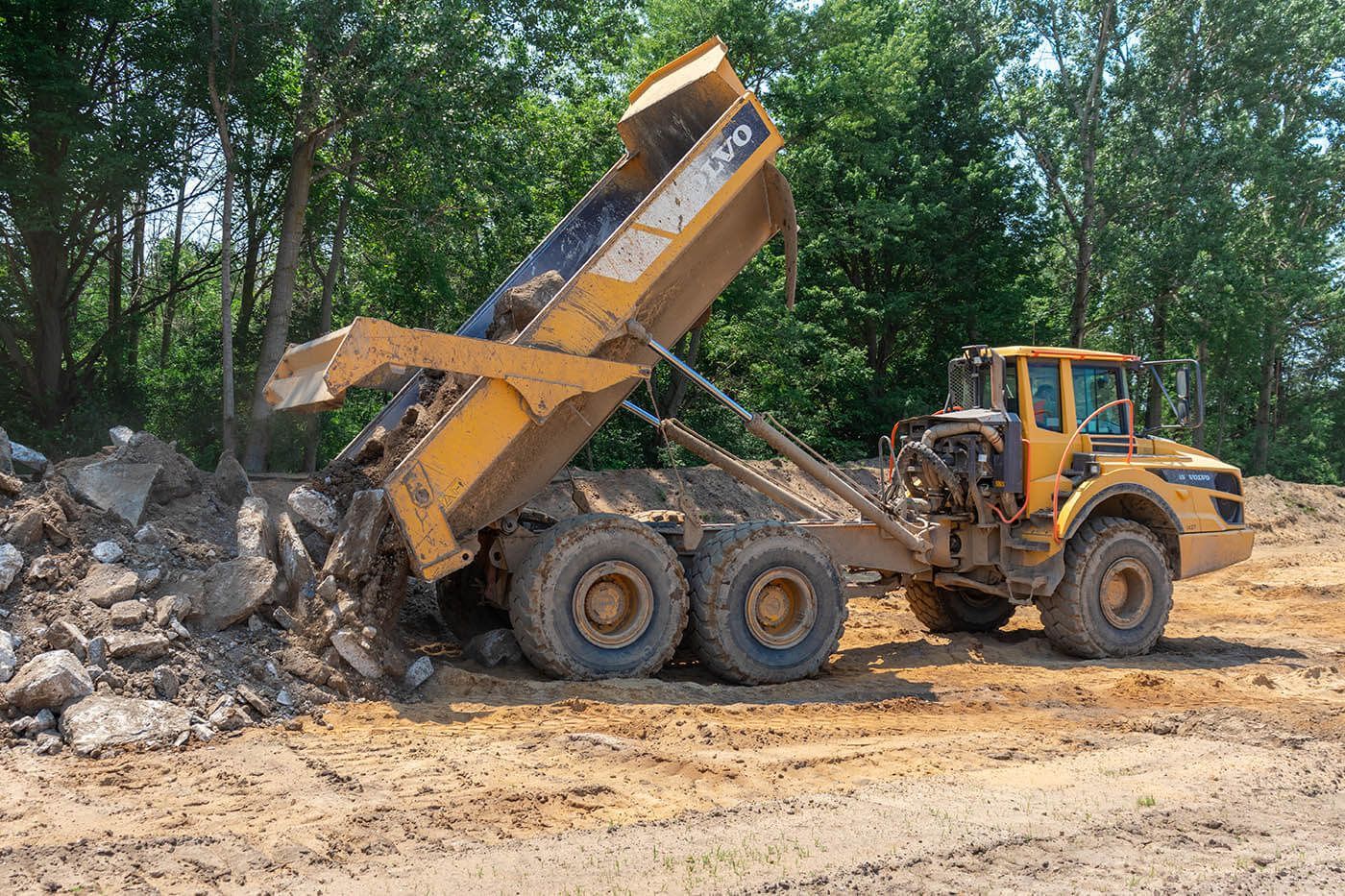 A yellow dump truck is sitting on top of a dirt field.