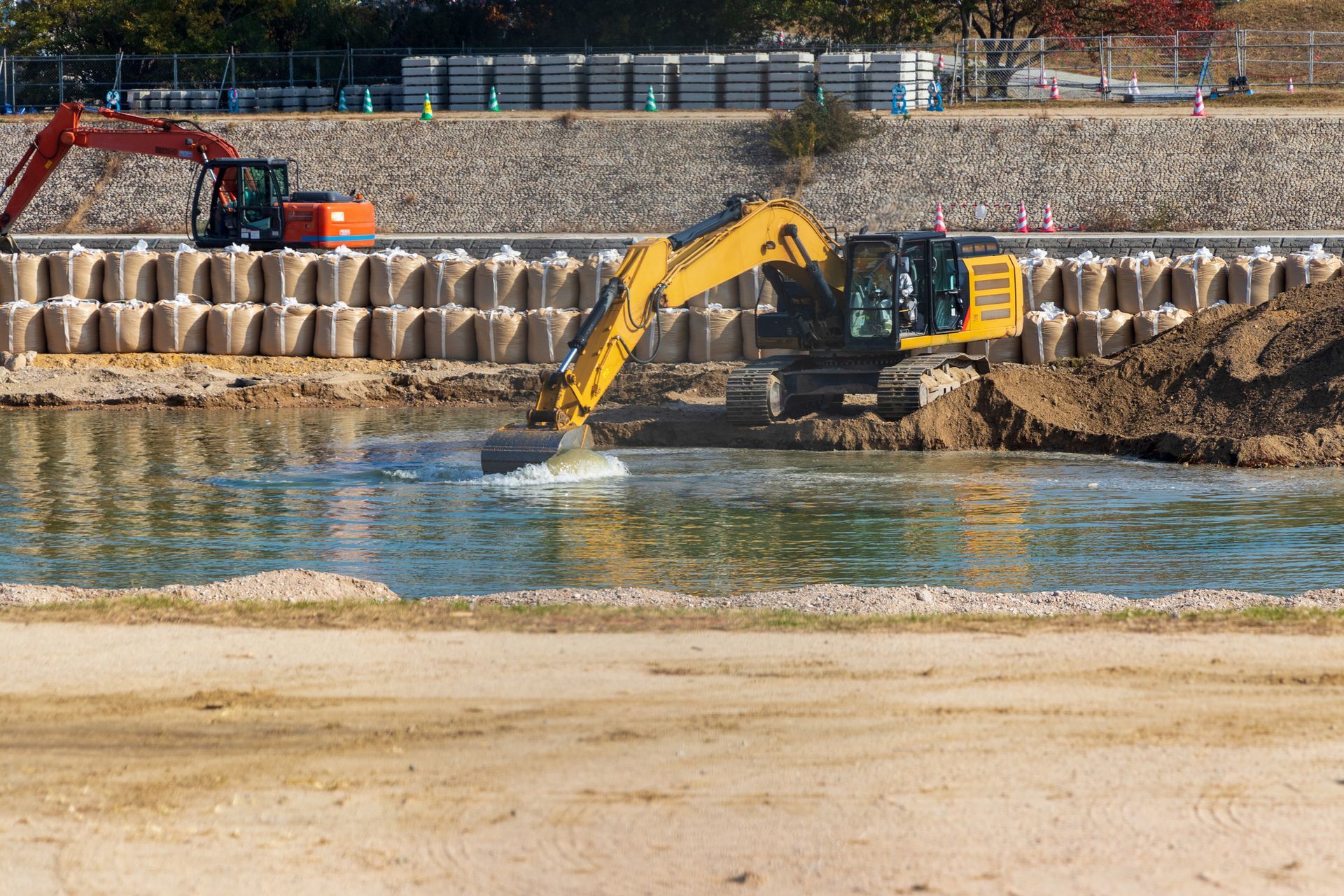 A yellow excavator is digging a hole in the water.