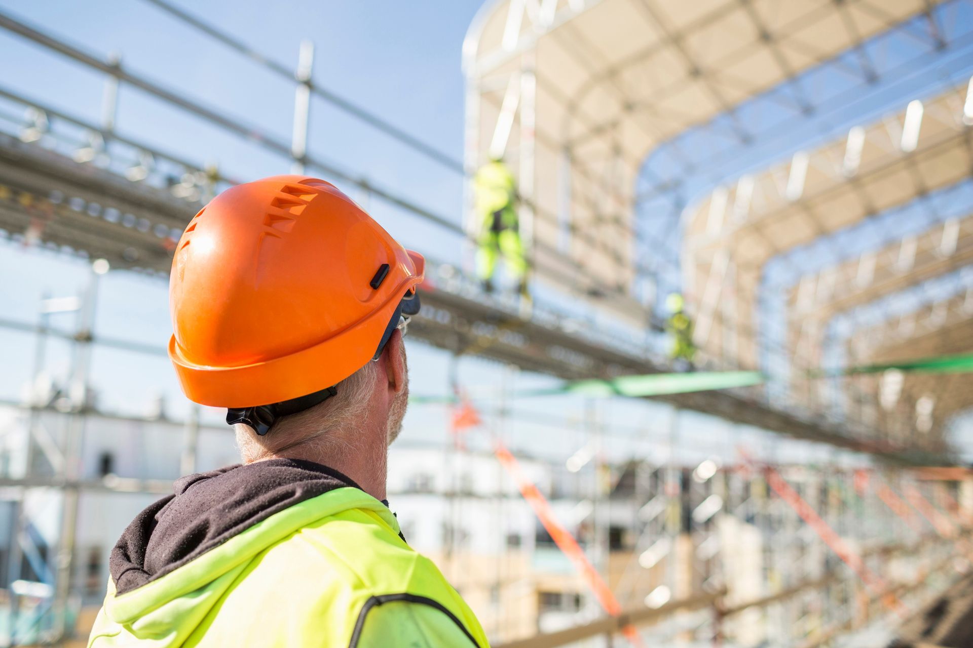A construction worker wearing an orange hard hat is looking at a building under construction.