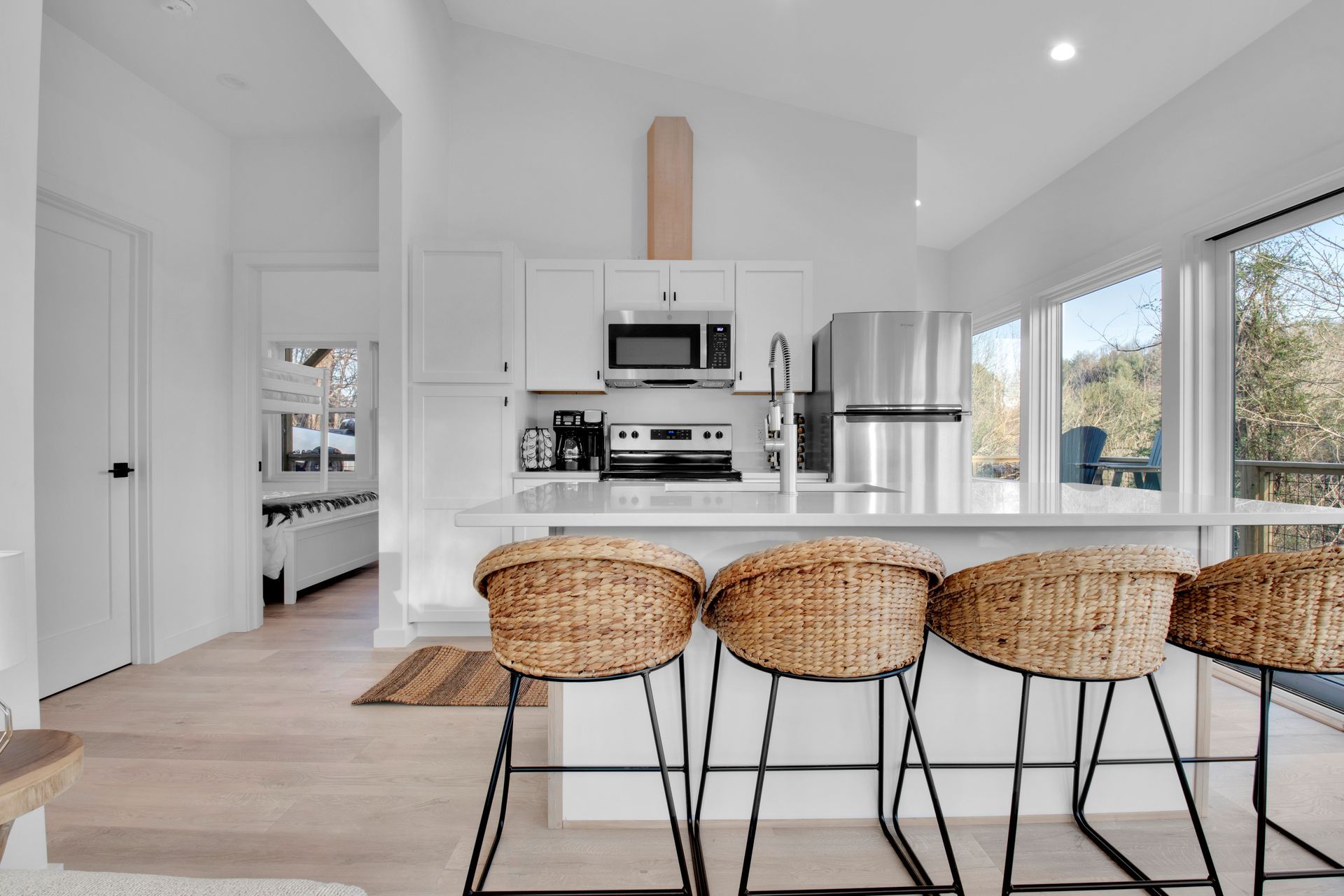 A kitchen with white cabinets , stainless steel appliances , and wicker bar stools.