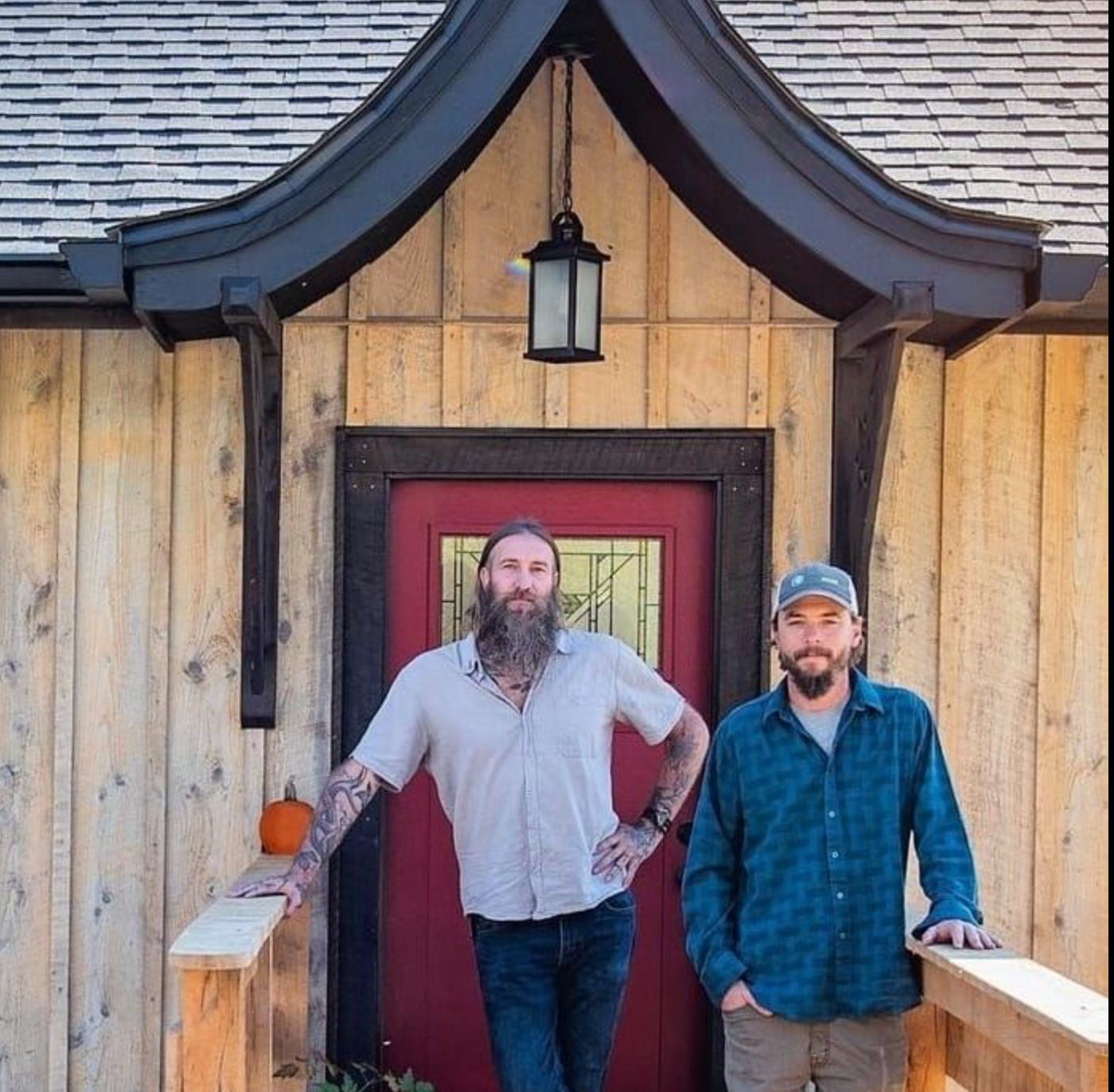 Two men standing in front of a wooden house with a red door