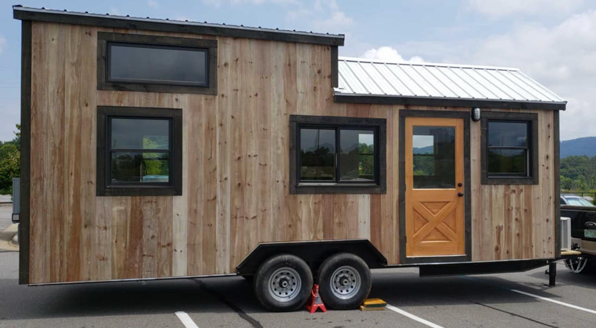 A small wooden house on wheels is parked in a parking lot.