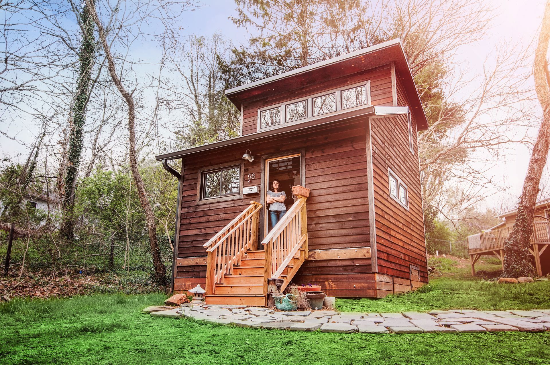 A woman is standing on the steps of a small wooden house.
