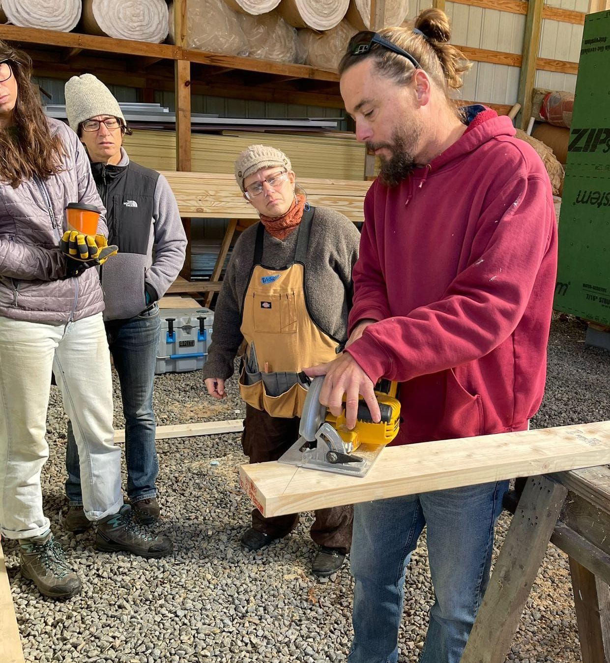 A group of people are standing around a man cutting a piece of wood.