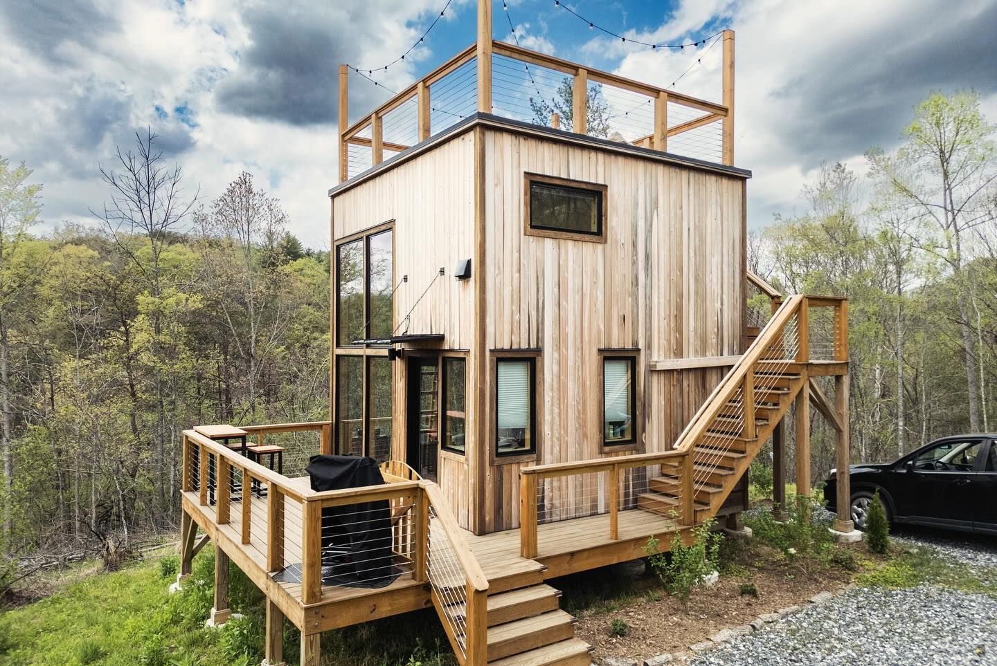 Rustic cabin with a stone fire pit, wooden deck, and surrounding trees.