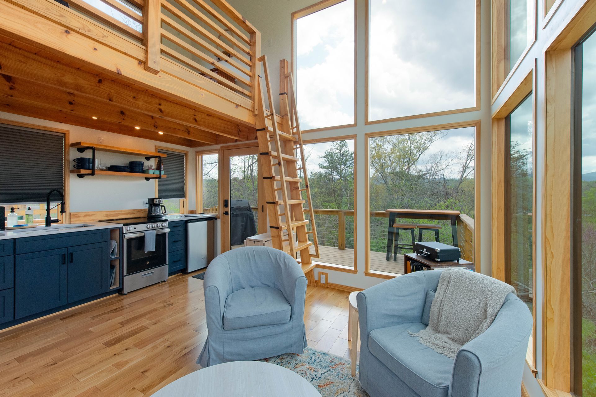 A living room with two chairs , a table , a ladder and a kitchen.