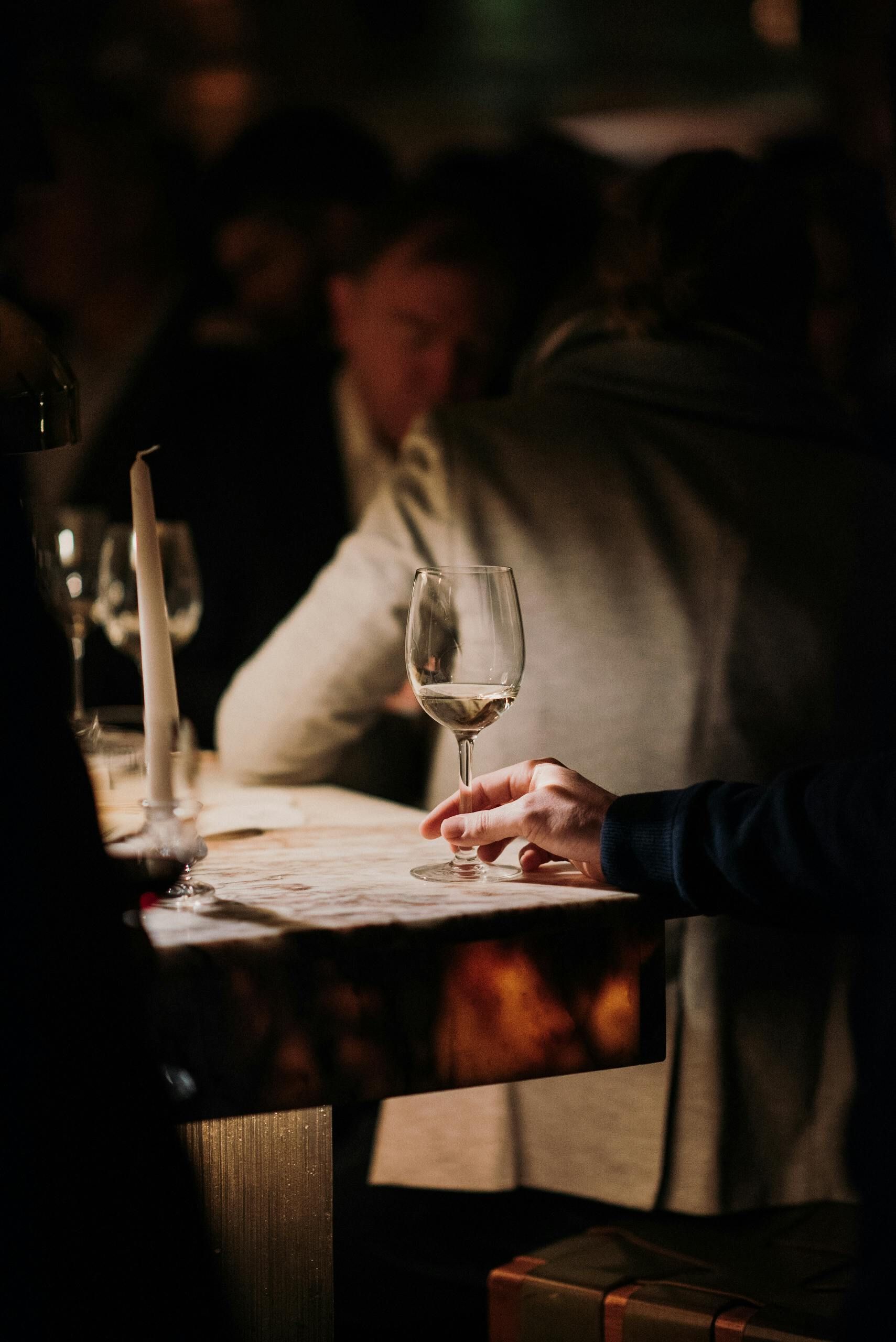 Person holding wine bottle and glass of red wine outside.