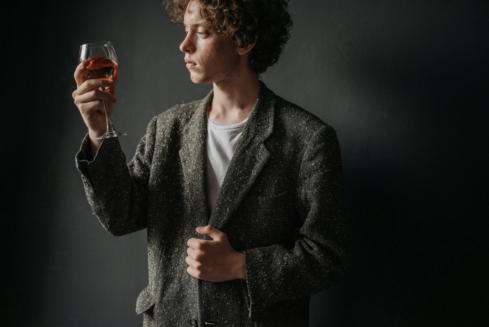 Person in patterned blazer examines a glass of wine, against a dark gray background.