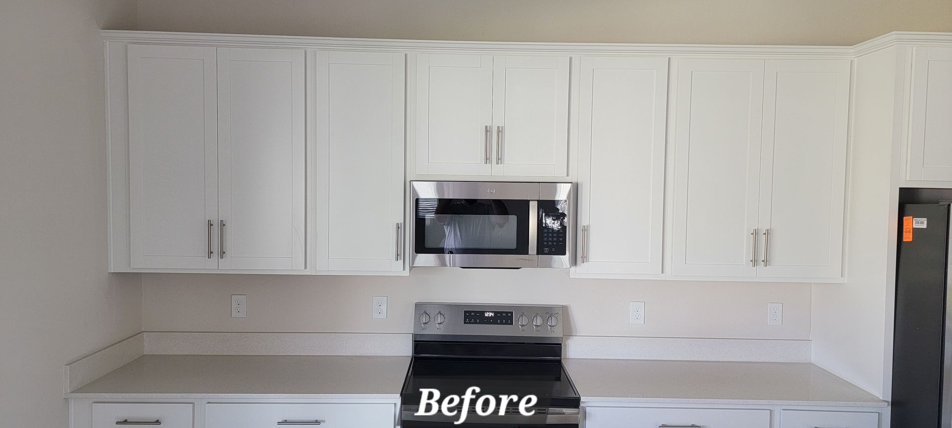 A kitchen with white cabinets , a stove , microwave and refrigerator.