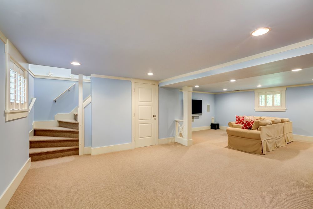 Finished basement with staircase, light blue walls, tan carpet, and beige sofa.