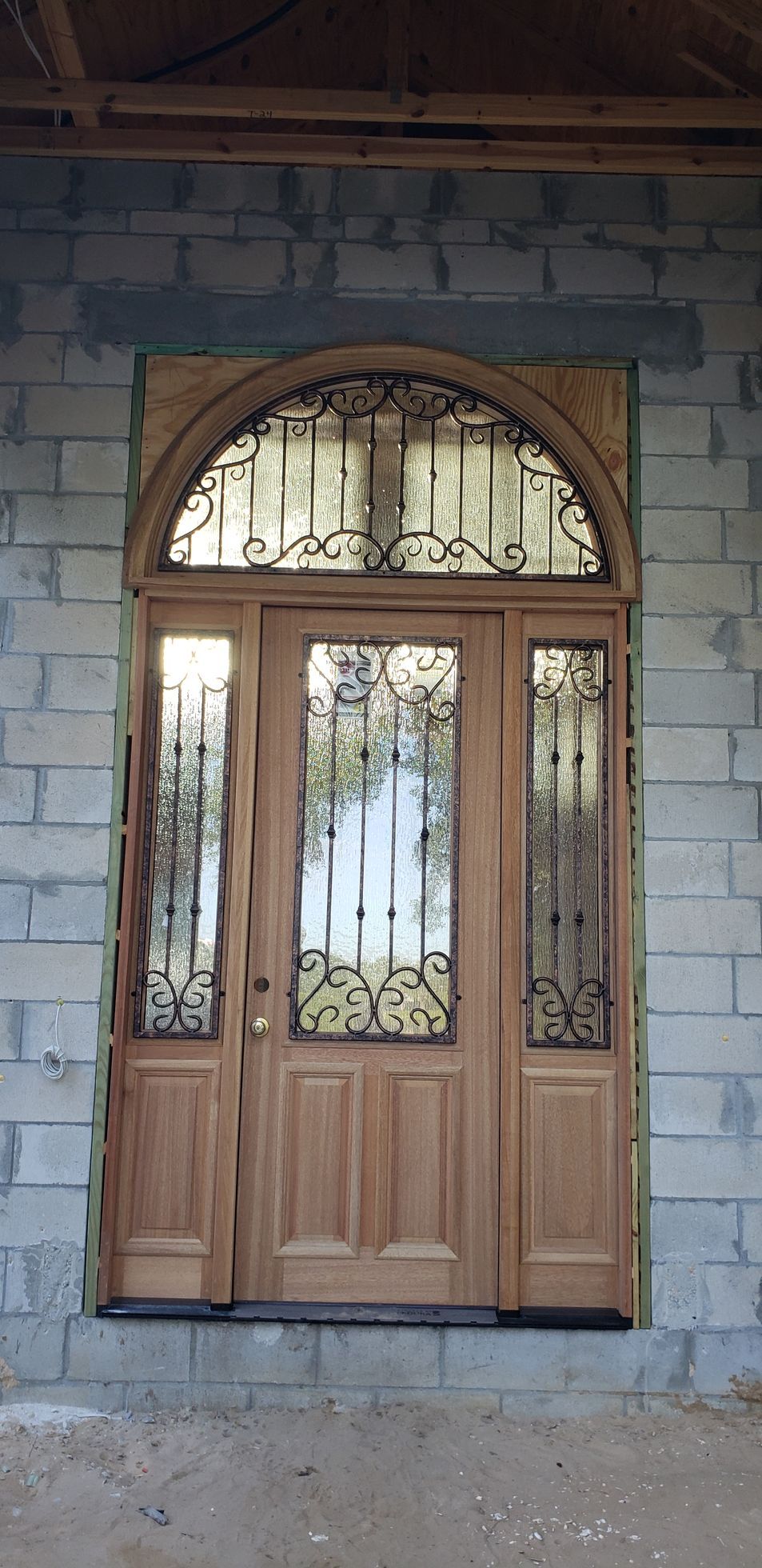 A wooden door with a wrought iron window is on a brick wall.