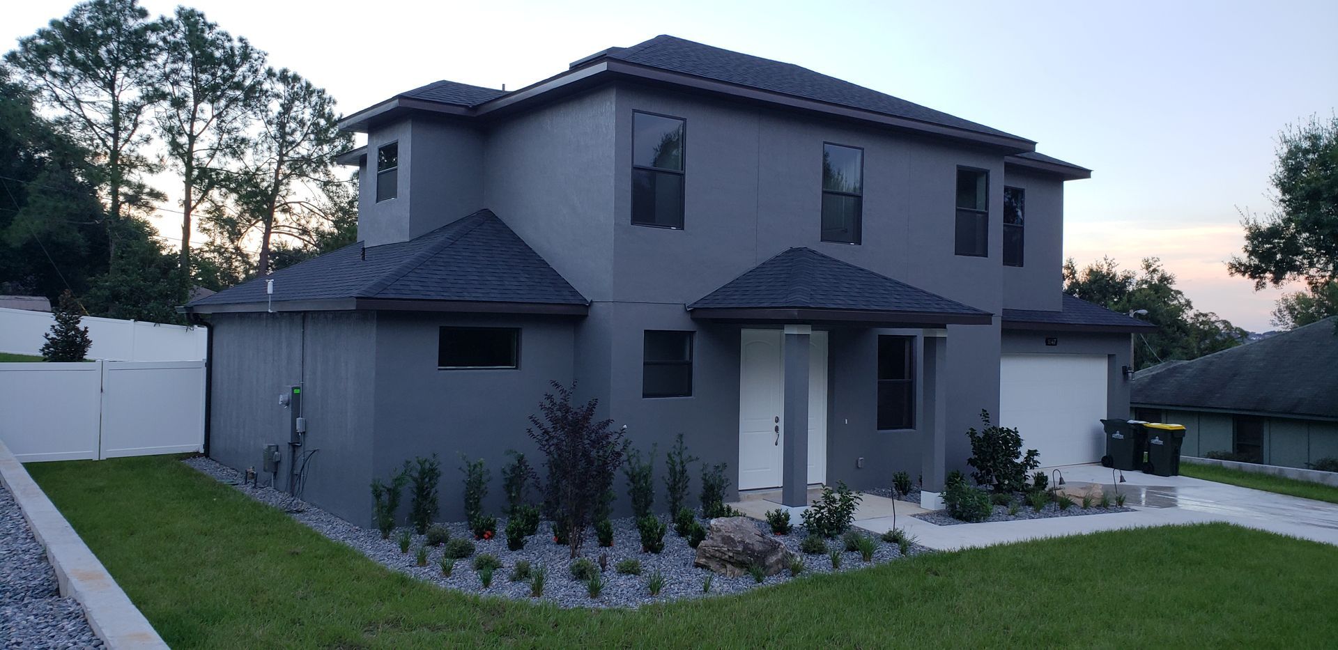 A large gray house with a black roof is sitting on top of a lush green lawn.
