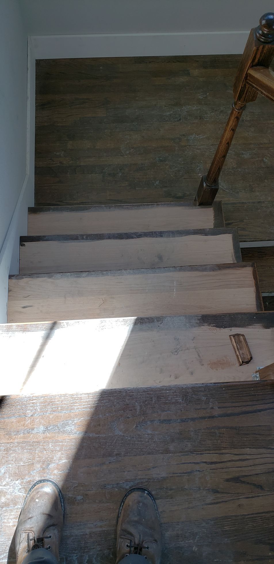 A person is standing on a wooden floor next to a set of stairs.