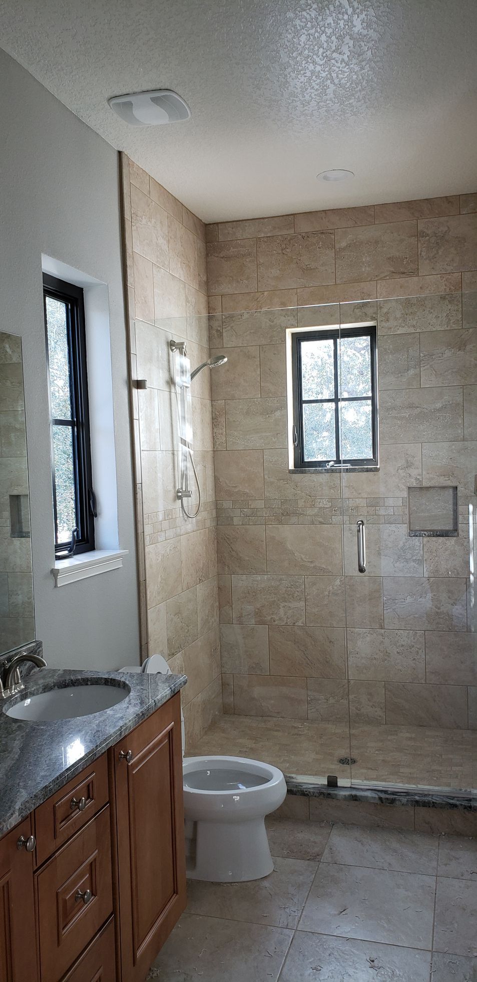 A bathroom with a toilet , sink , shower and window.