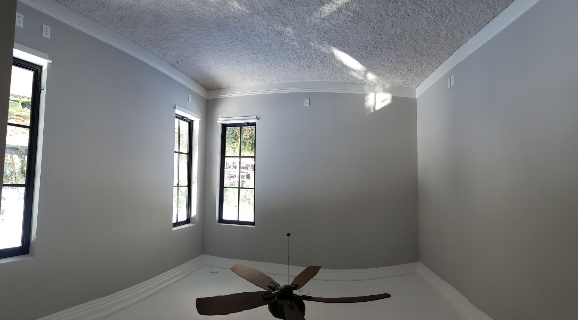 An empty room with a ceiling fan and two windows
