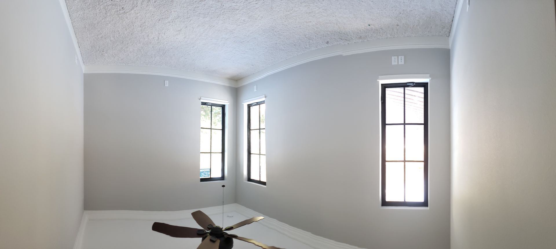 An empty room with a ceiling fan and two windows.