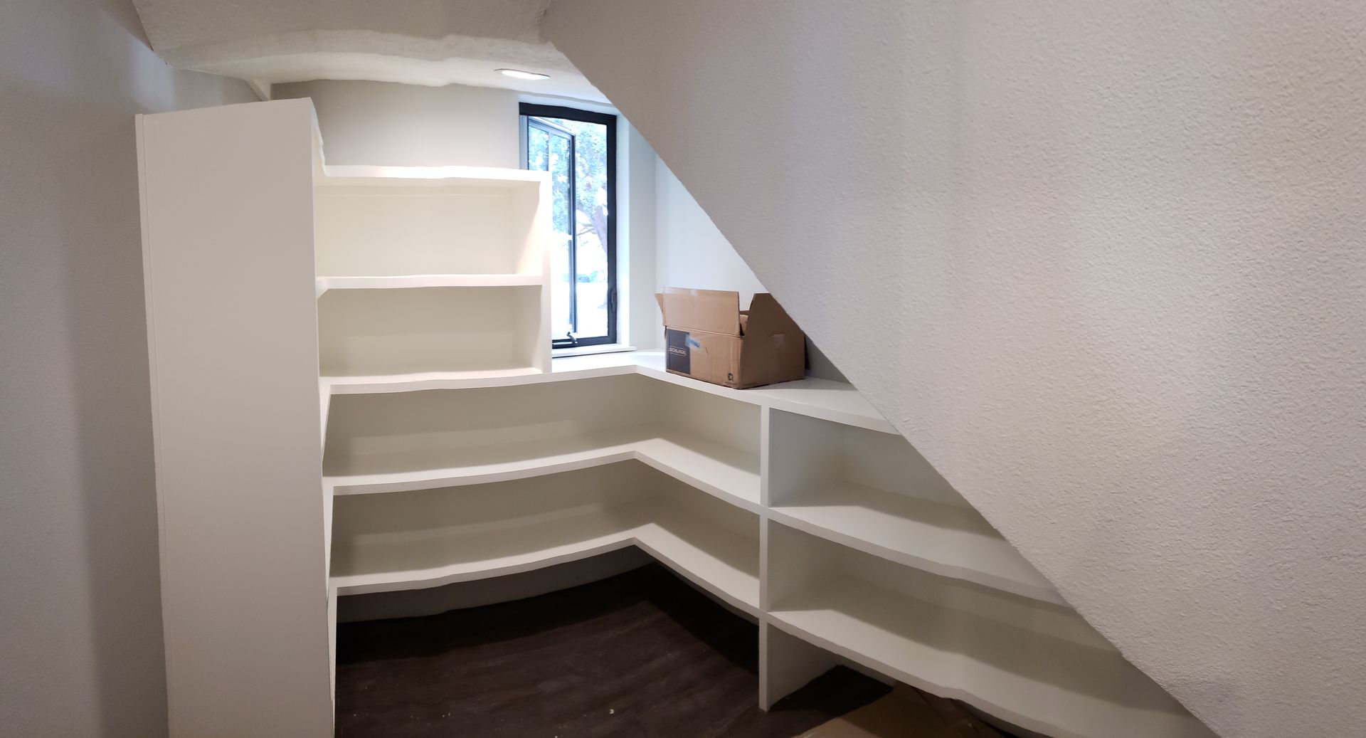 A room with a staircase and shelves underneath it.