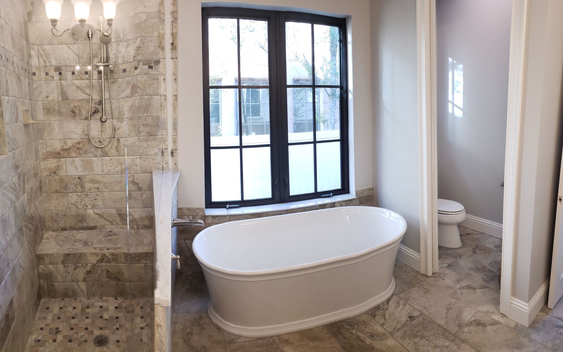 A bathroom with a tub , toilet , shower and window.
