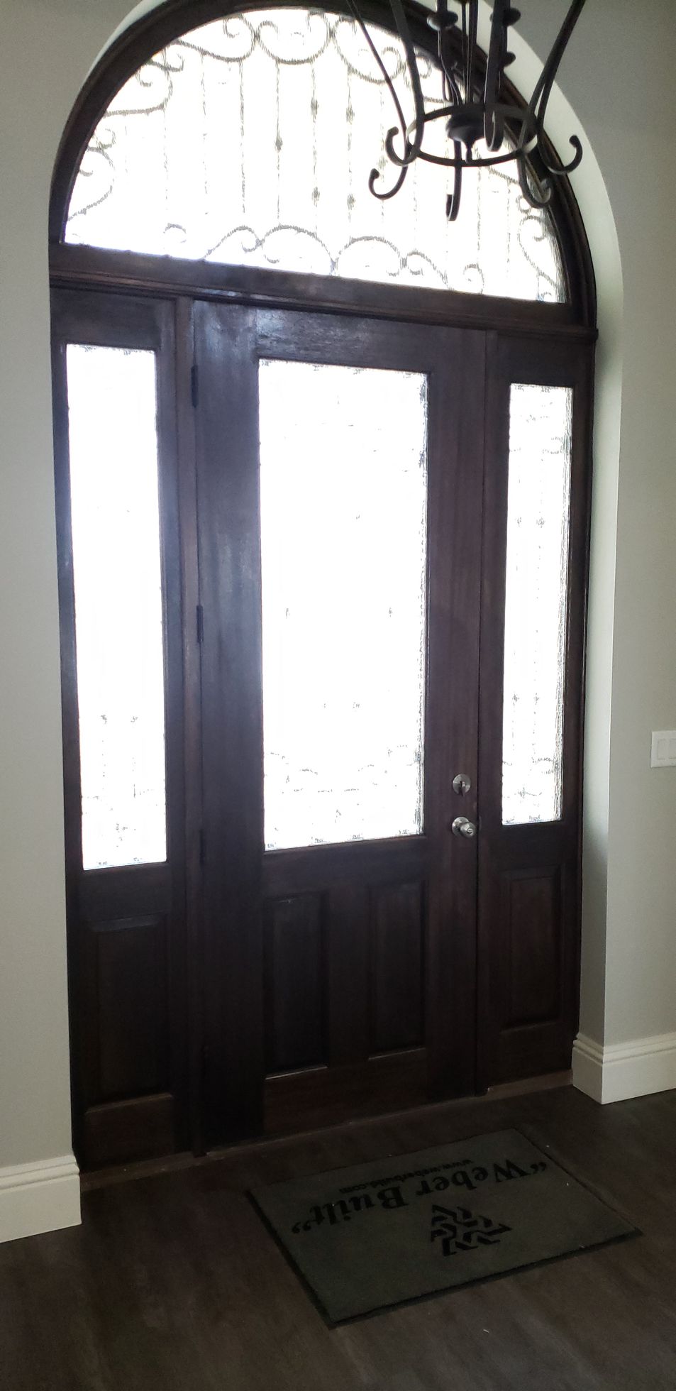 A door with a chandelier above it and a door mat in front of it.