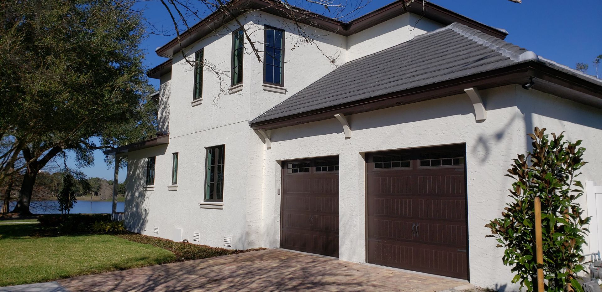 A white house with a brown garage door is sitting next to a body of water.