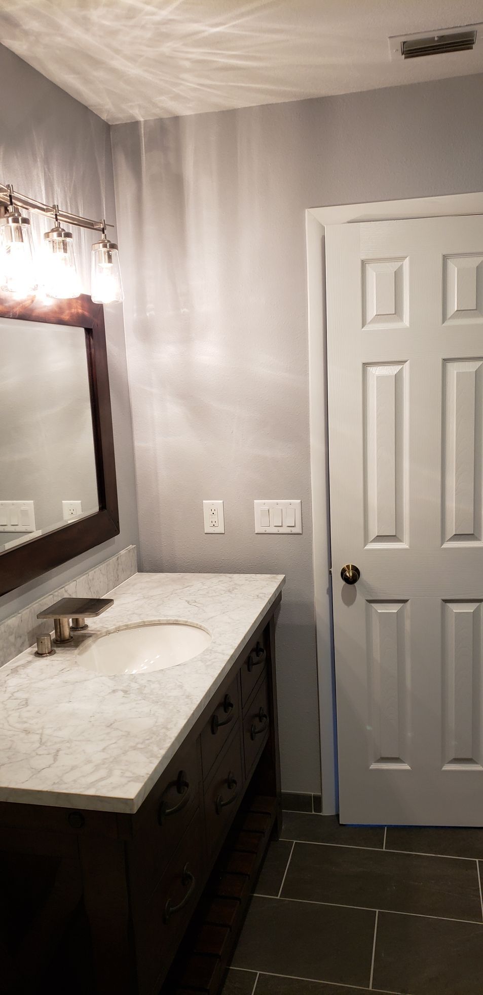 A bathroom with a sink , mirror and door.