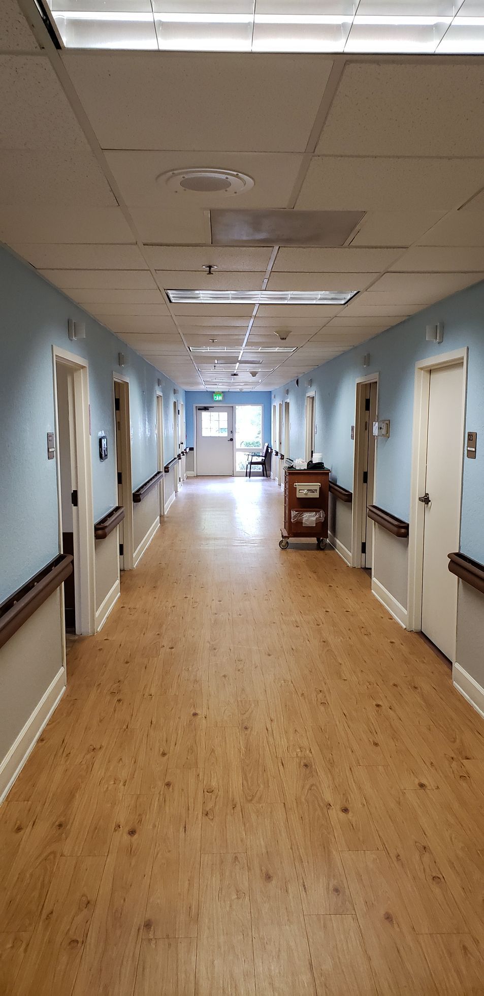 A long hallway in a hospital with wooden floors and blue walls.