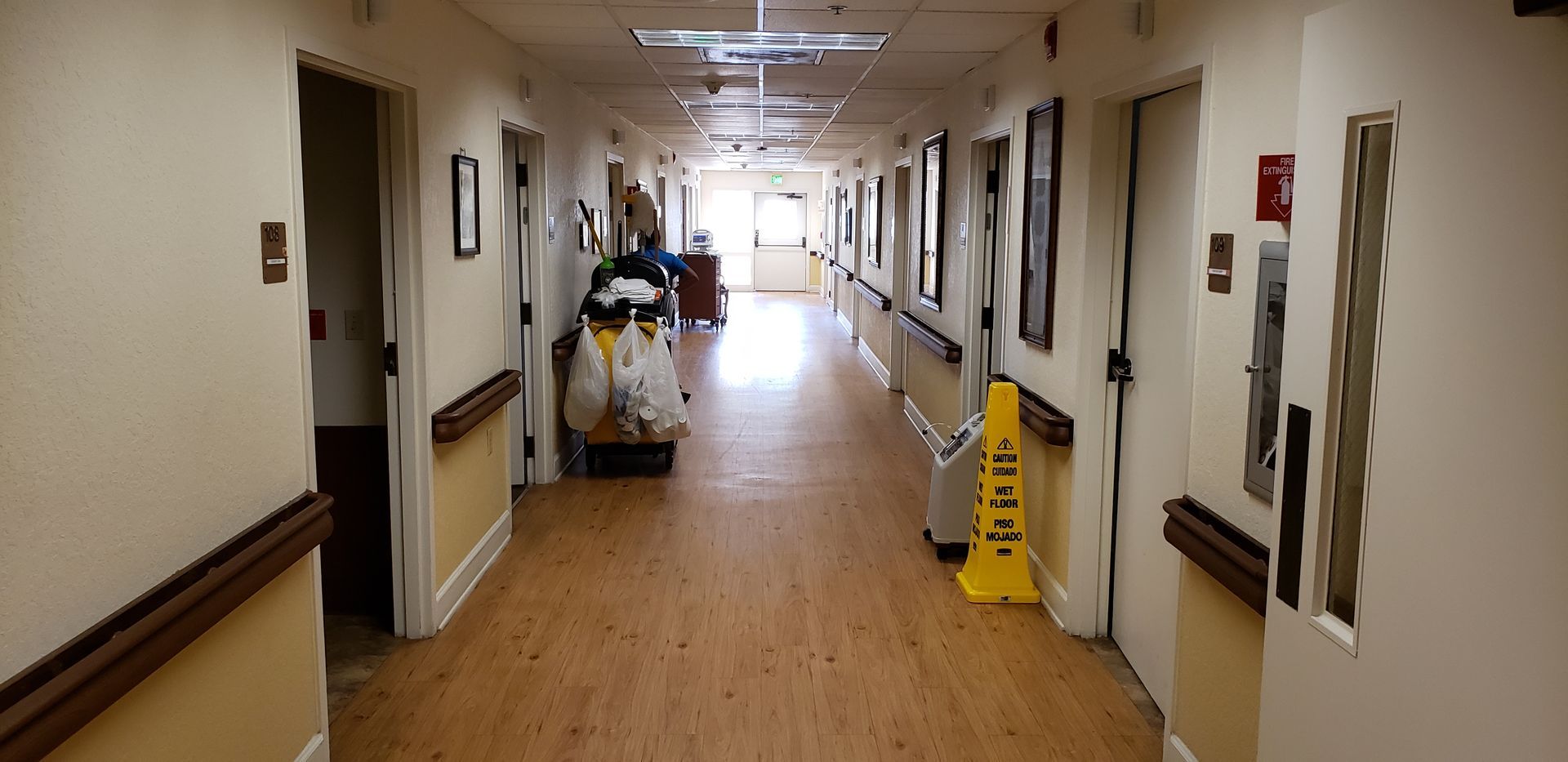 A long hallway in a hospital with a yellow wet floor sign