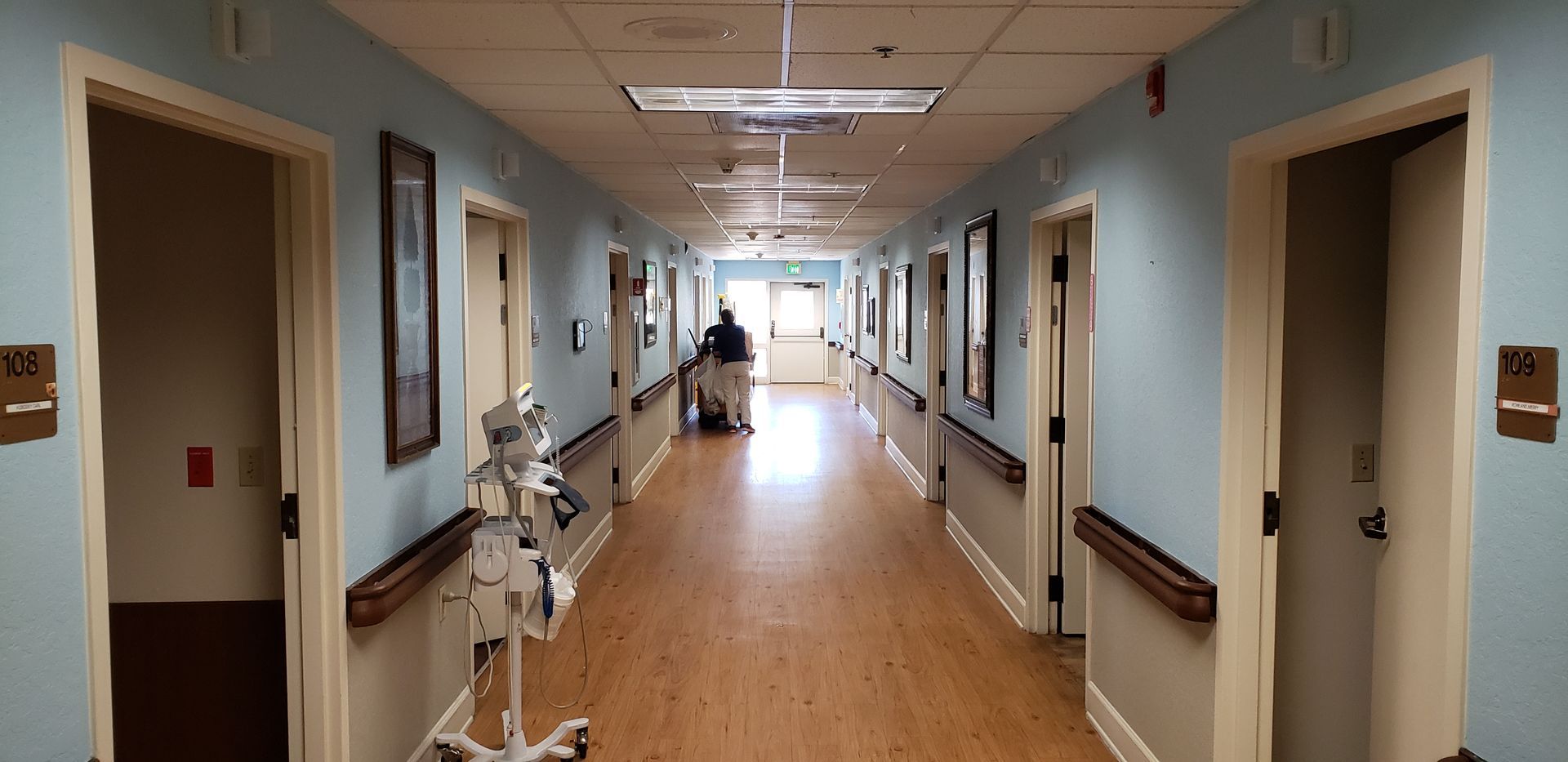 A long hallway in a hospital with a man walking down it.