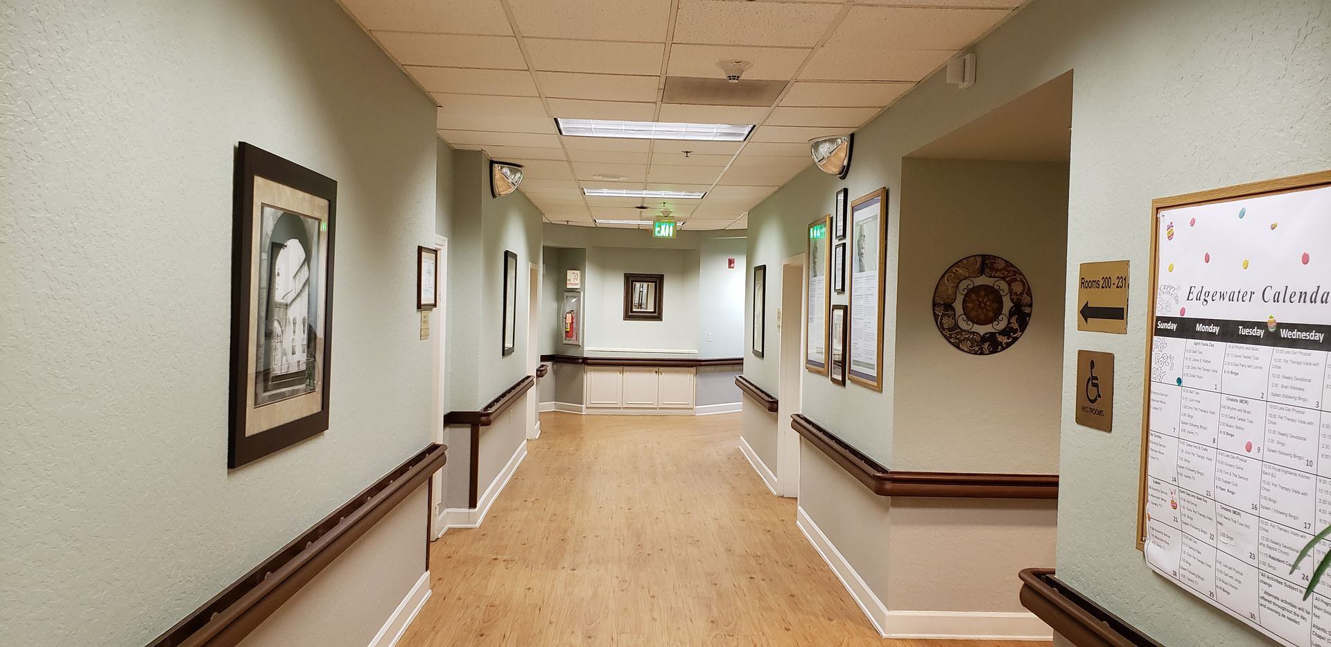 A long hallway with wooden floors and a bulletin board on the wall