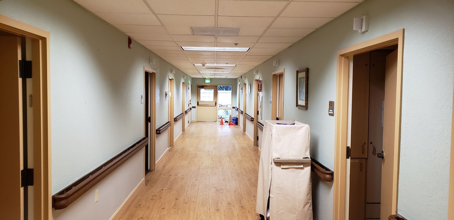 A long hallway with wooden floors and doors in a hospital