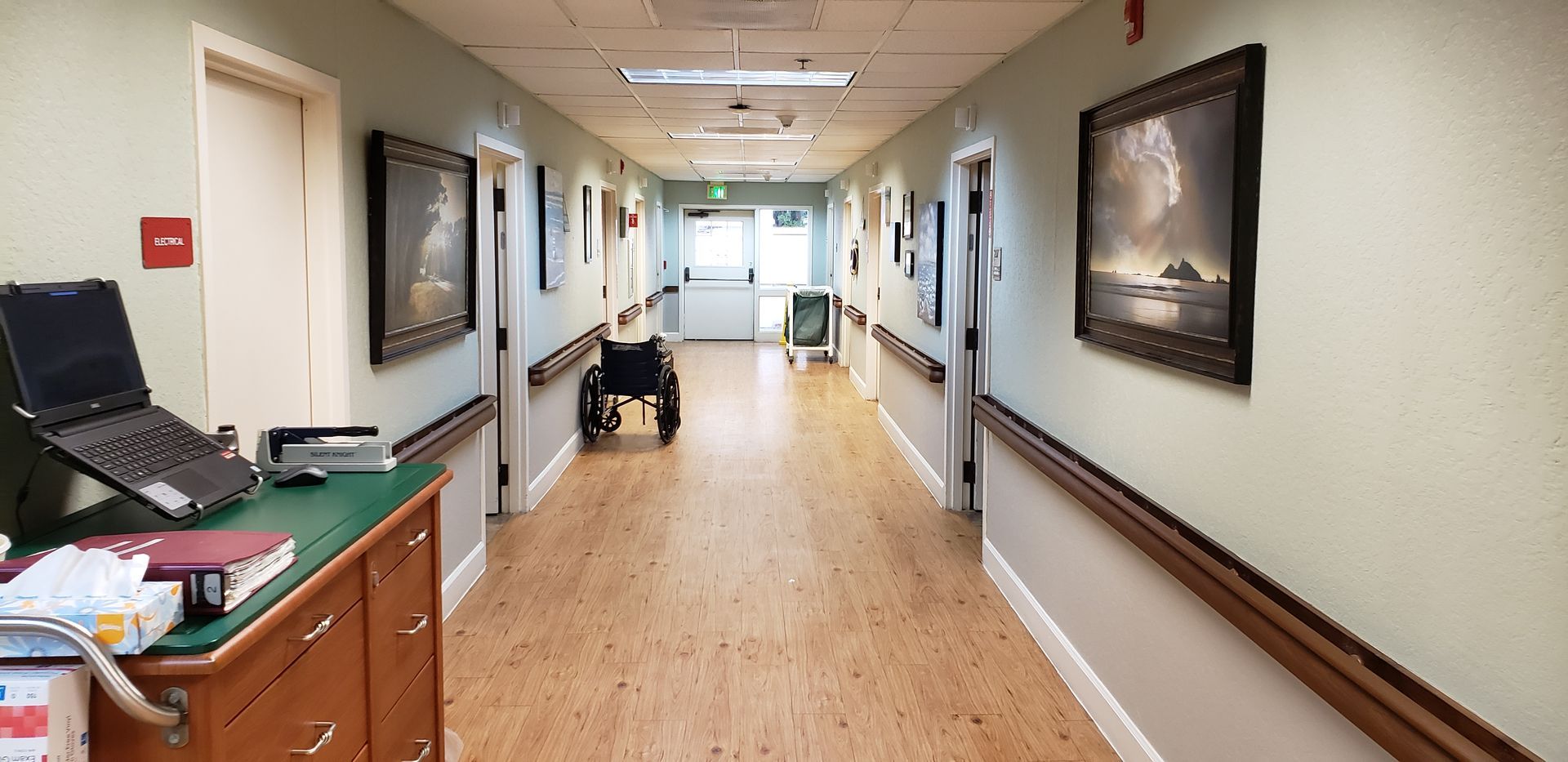 A long hallway in a hospital with a wheelchair in the middle.