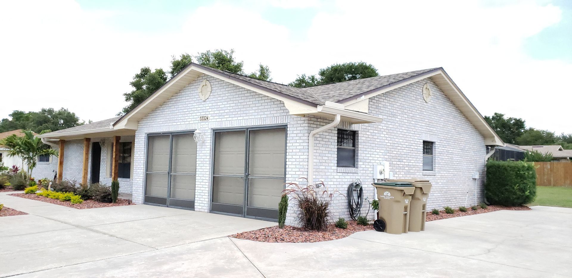 A white house with a garage and a trash can in front of it.