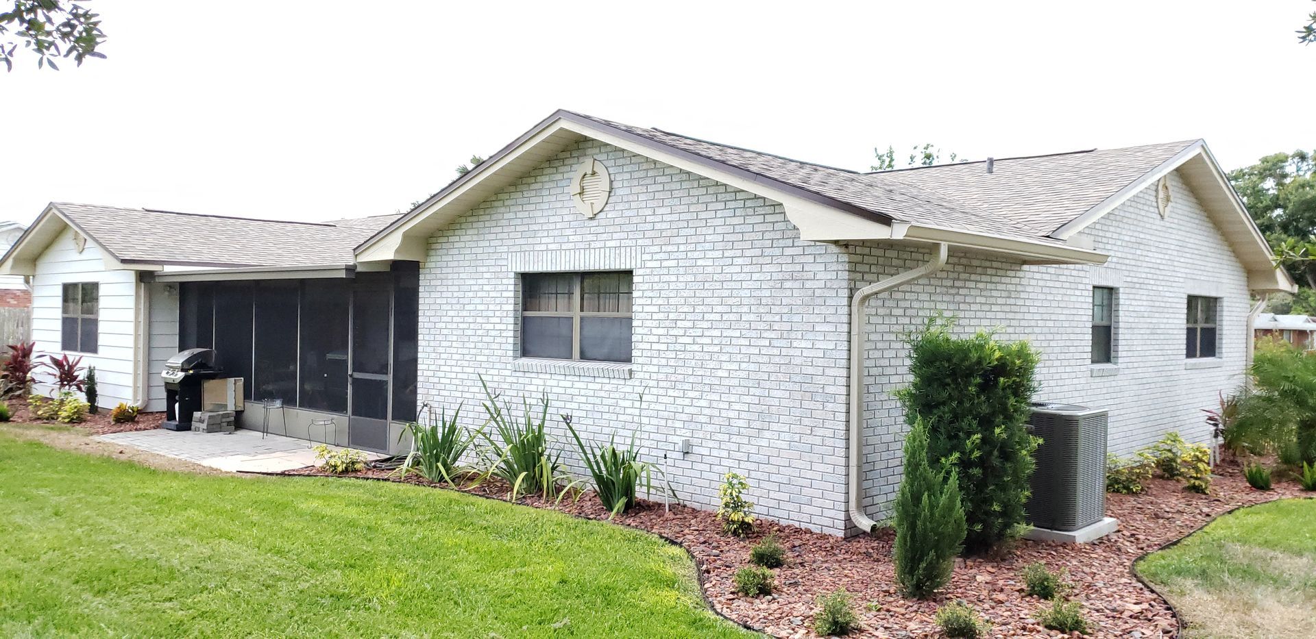 A white brick house with a gray roof and a screened in porch.