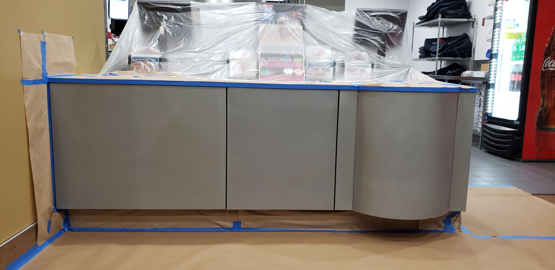 A counter is being painted in a store with blue tape.