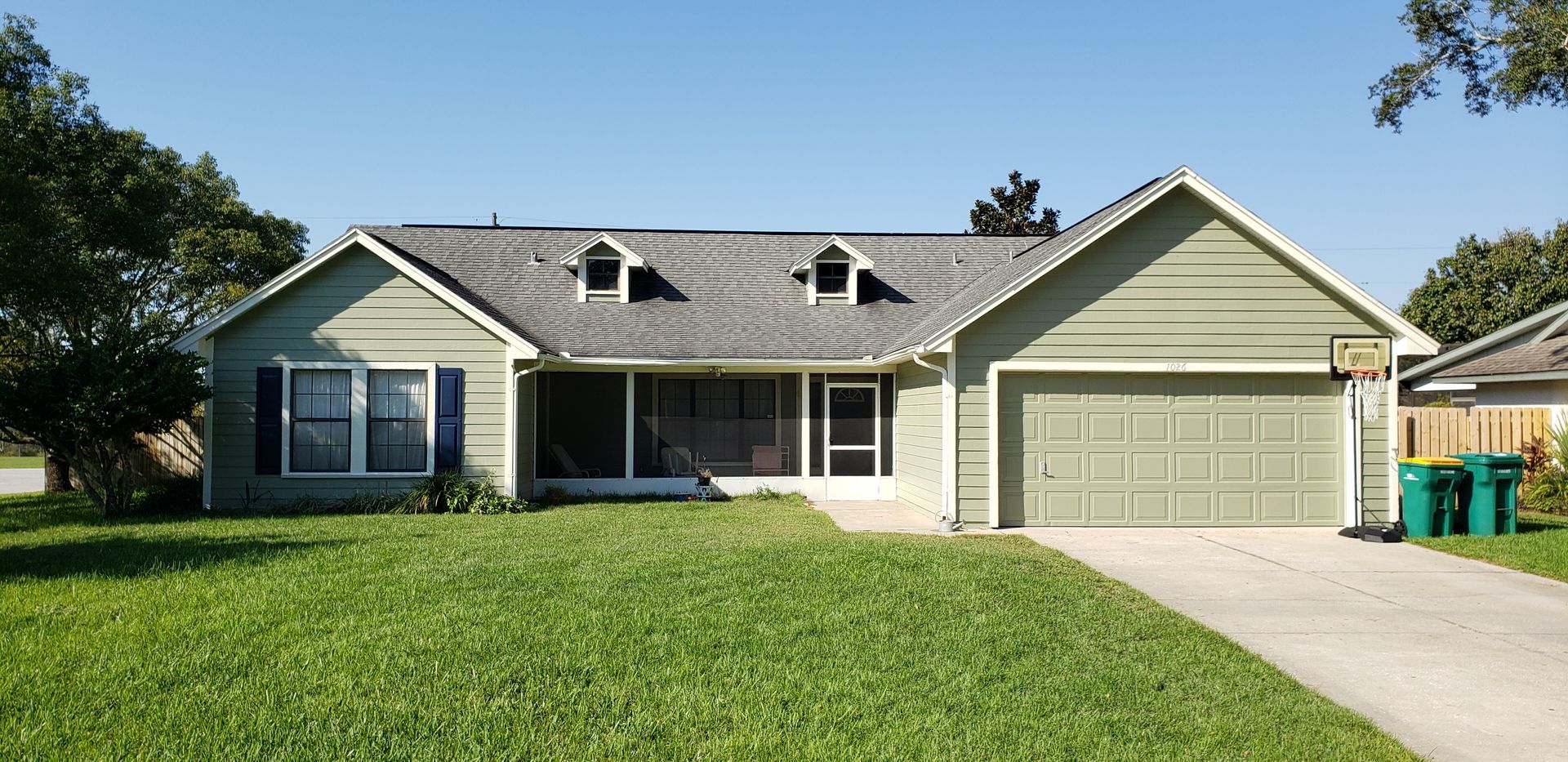 A house with a green garage door and green trash cans in front of it
